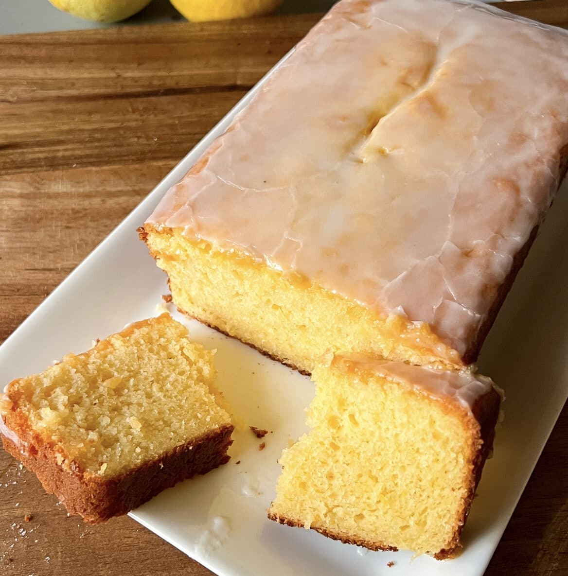 A delicious lemon loaf cake in a plate with a slice broken in half. The cake is yellow in colour.