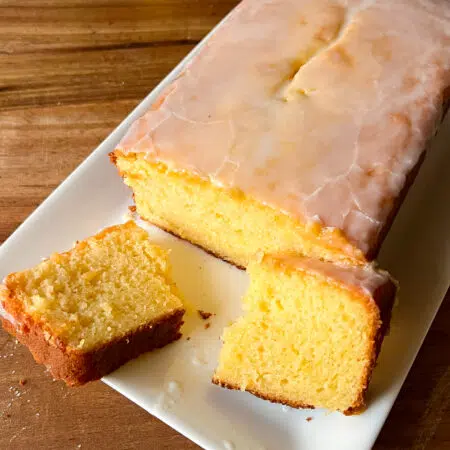 A delicious lemon loaf cake in a plate with a slice broken in half. The cake is yellow in colour.