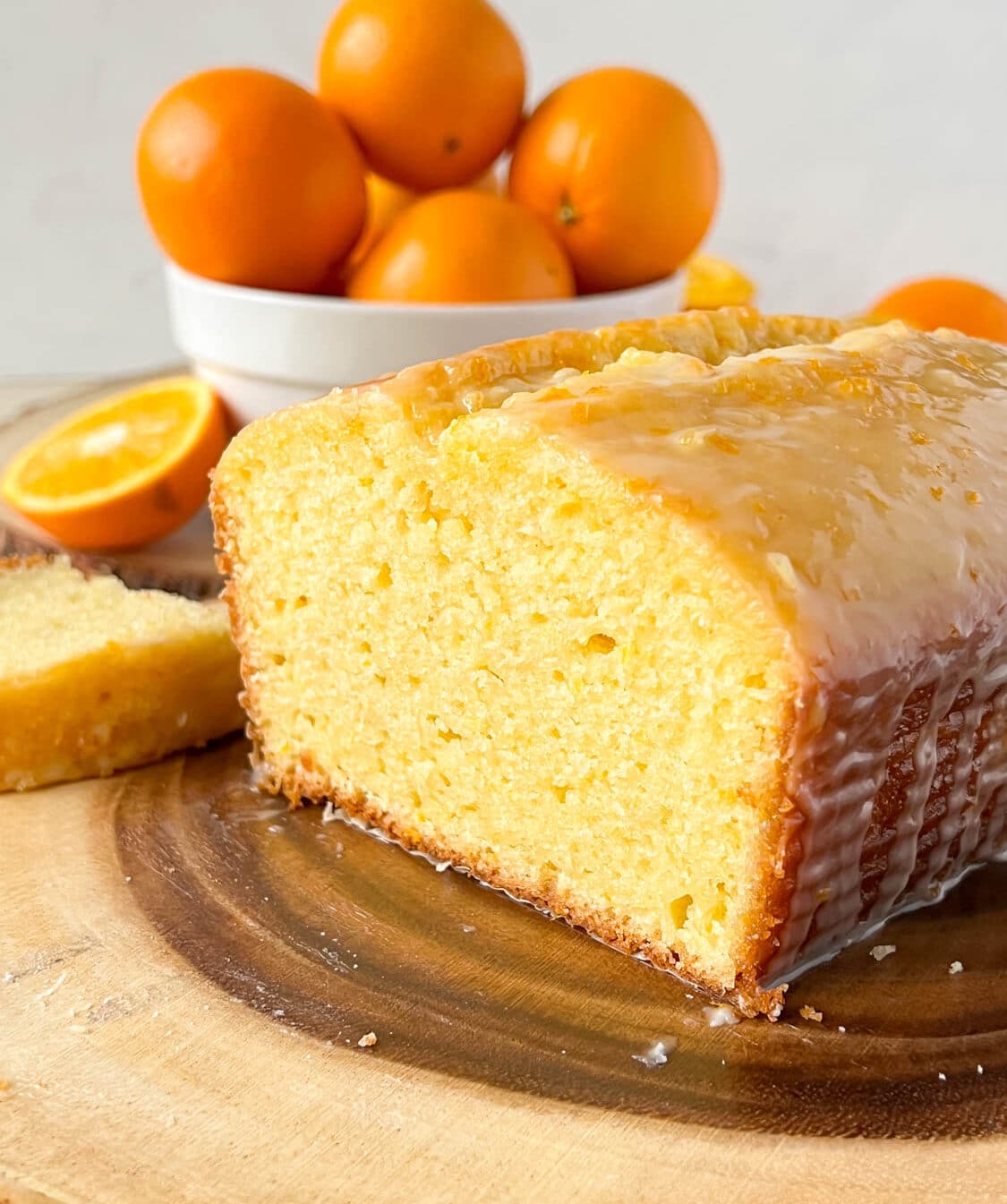 orange loaf cake cut in half on a wooden board, with oranges in the back