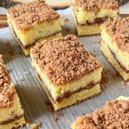 A slice of cinnamon coffee cake on an off white surface, surrounded by more slices of cake