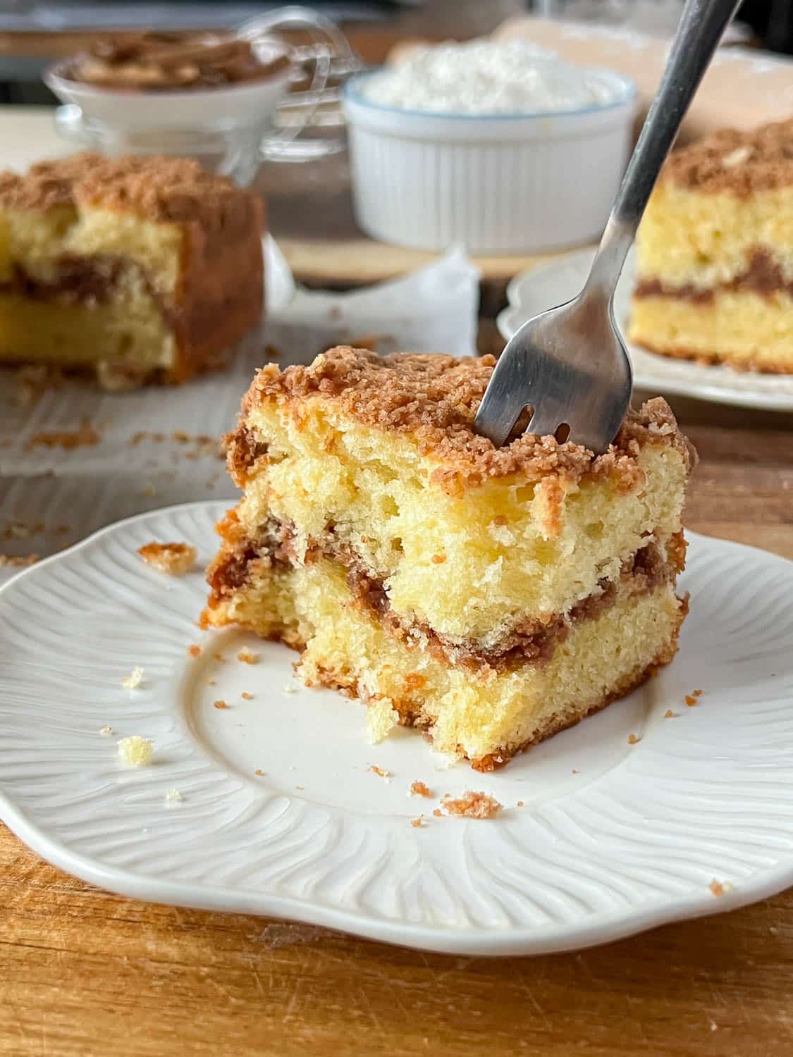 A plate with a slice of cinnamon coffee cake with a fork cutting into it