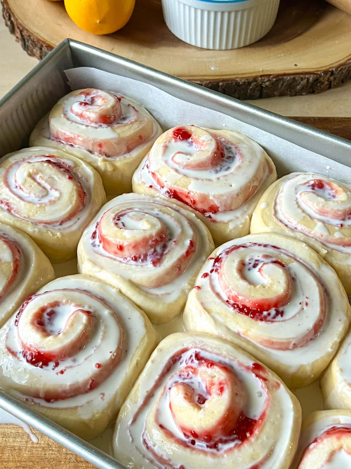 Unbaked raspberry lemon rolls in a pan, covered with heavy cream