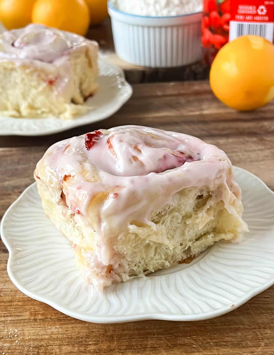 Raspberry Lemon roll in a white plate. The roll is covered with pink frosting and the inside is reddish.

A lemon and another roll in the background