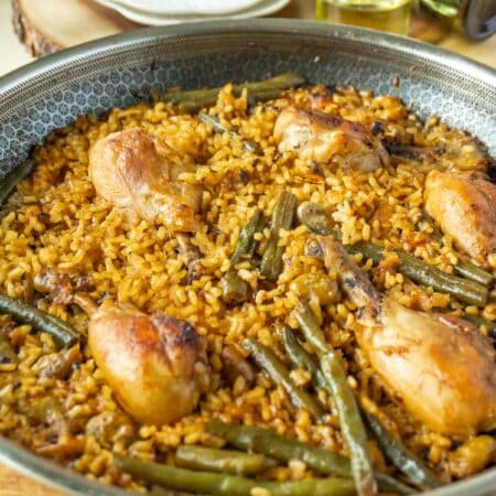 Paella valenciana (chicken paella) in a pan on a wooden cutting board