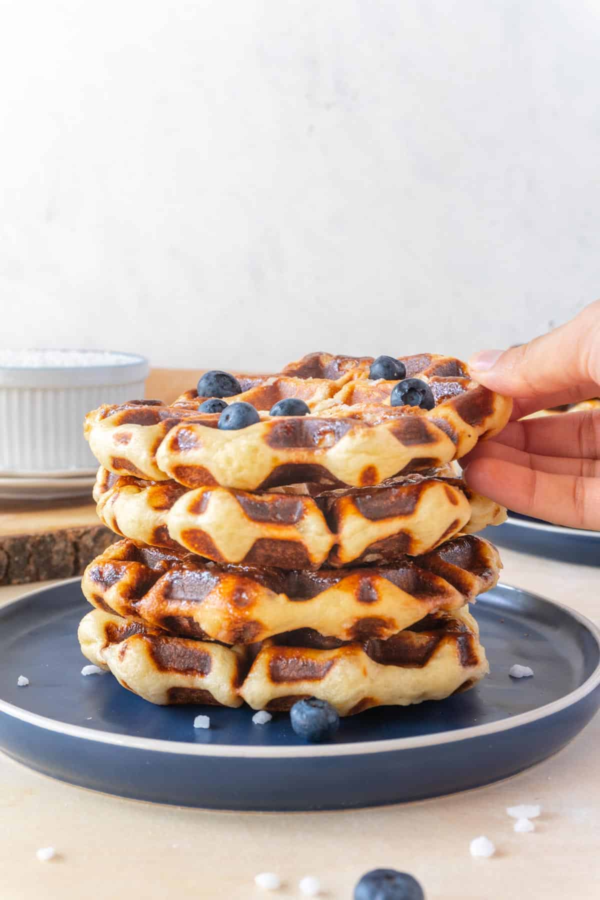 stack of liege waffles on a blue plate with a few blueberries on top