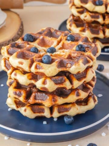 stack of liege waffles on a blue plate with a few blueberries on top