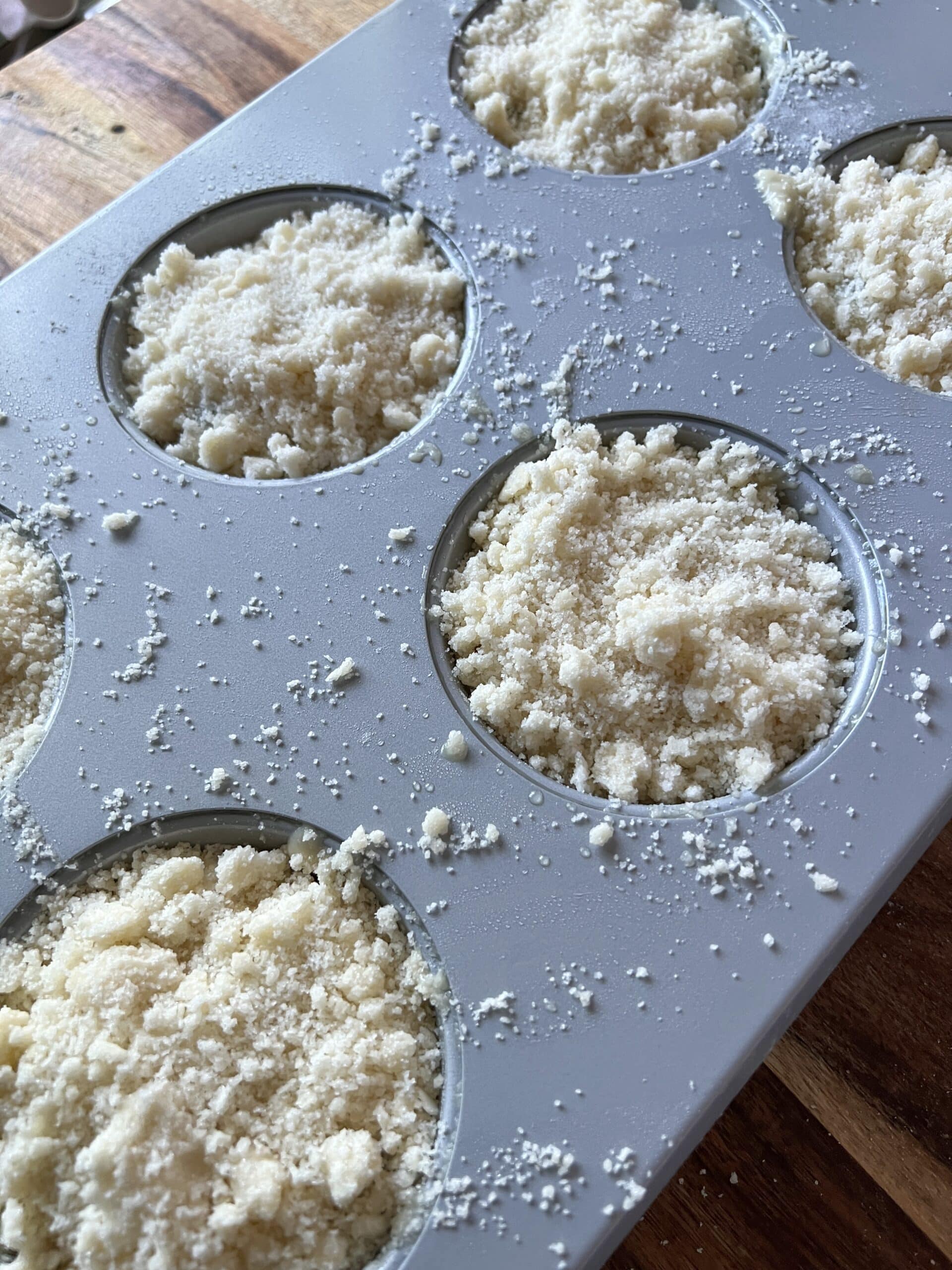 blueberry muffin batter covered in crumble in a muffin pan