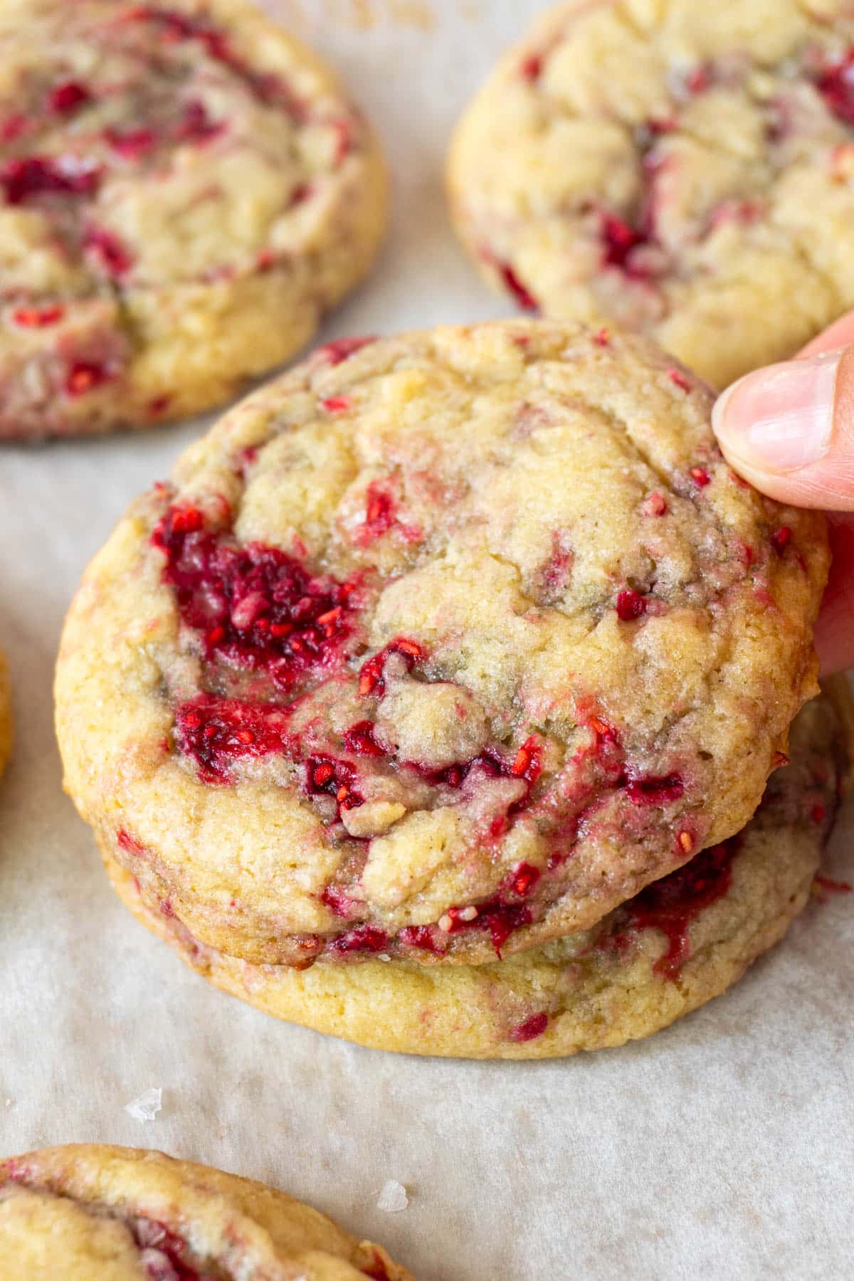 Two vanilla raspberry cookies stacked and a hand grabbing the top one