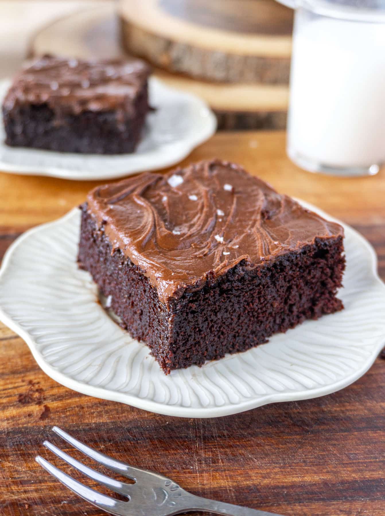 chocolate cake on a white plate, with a glass of milk in the back