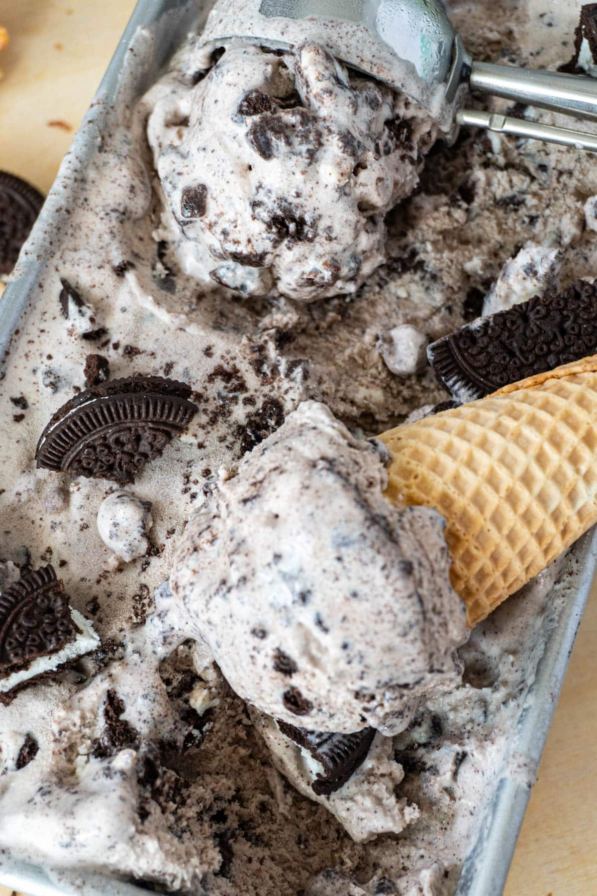 two scoops of cookies and cream ice cream in a container, one is in a cone