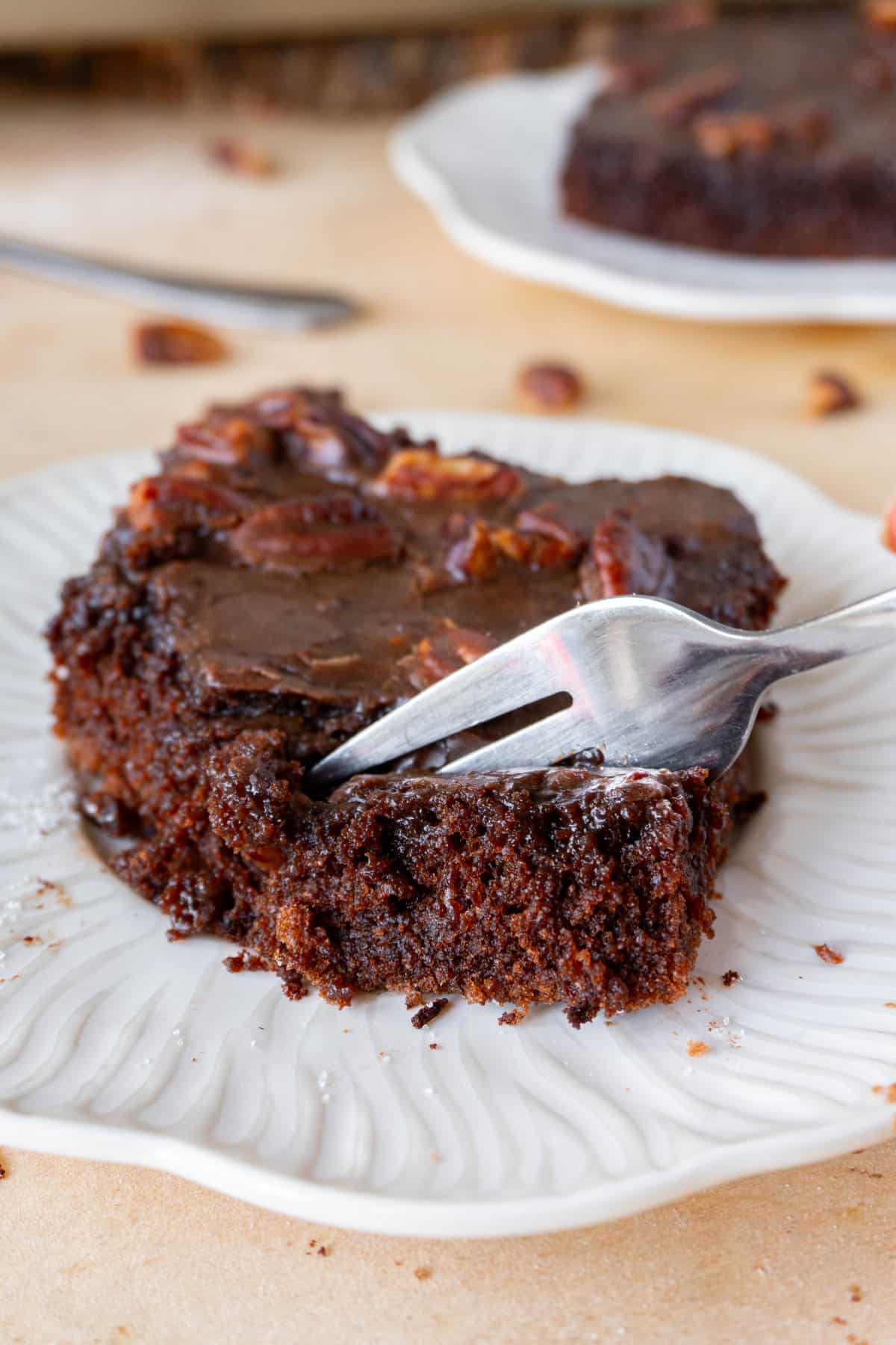 a slice of texas chocolate sheet cake in a white plate, being cut into with a fork