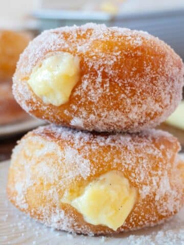 2 bomboloni or italian donuts stacked on a white plate