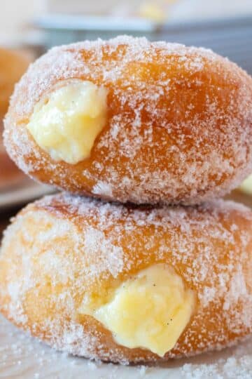 2 bomboloni or italian donuts stacked on a white plate