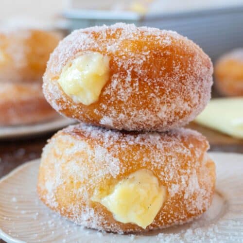 2 bomboloni or italian donuts stacked on a white plate