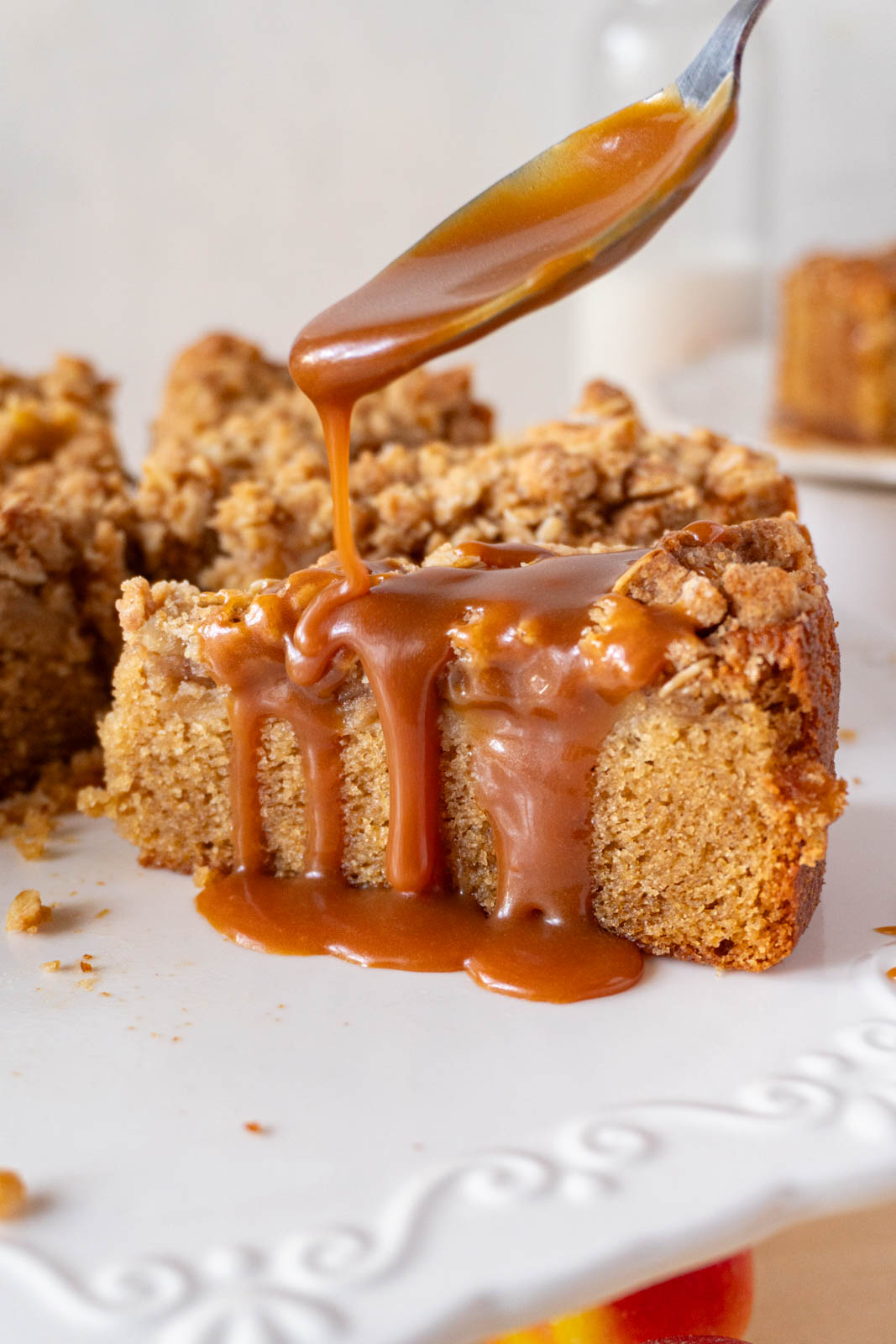 A slice of apple crumble cake, being drizzled with caramel sauce.