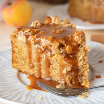 A slice of apple crumble cake, with a fork, on a white plate