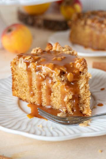 A slice of apple crumble cake, with a fork, on a white plate