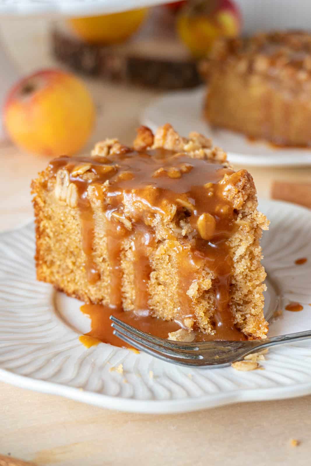 A slice of apple crumble cake, with a fork, on a white plate