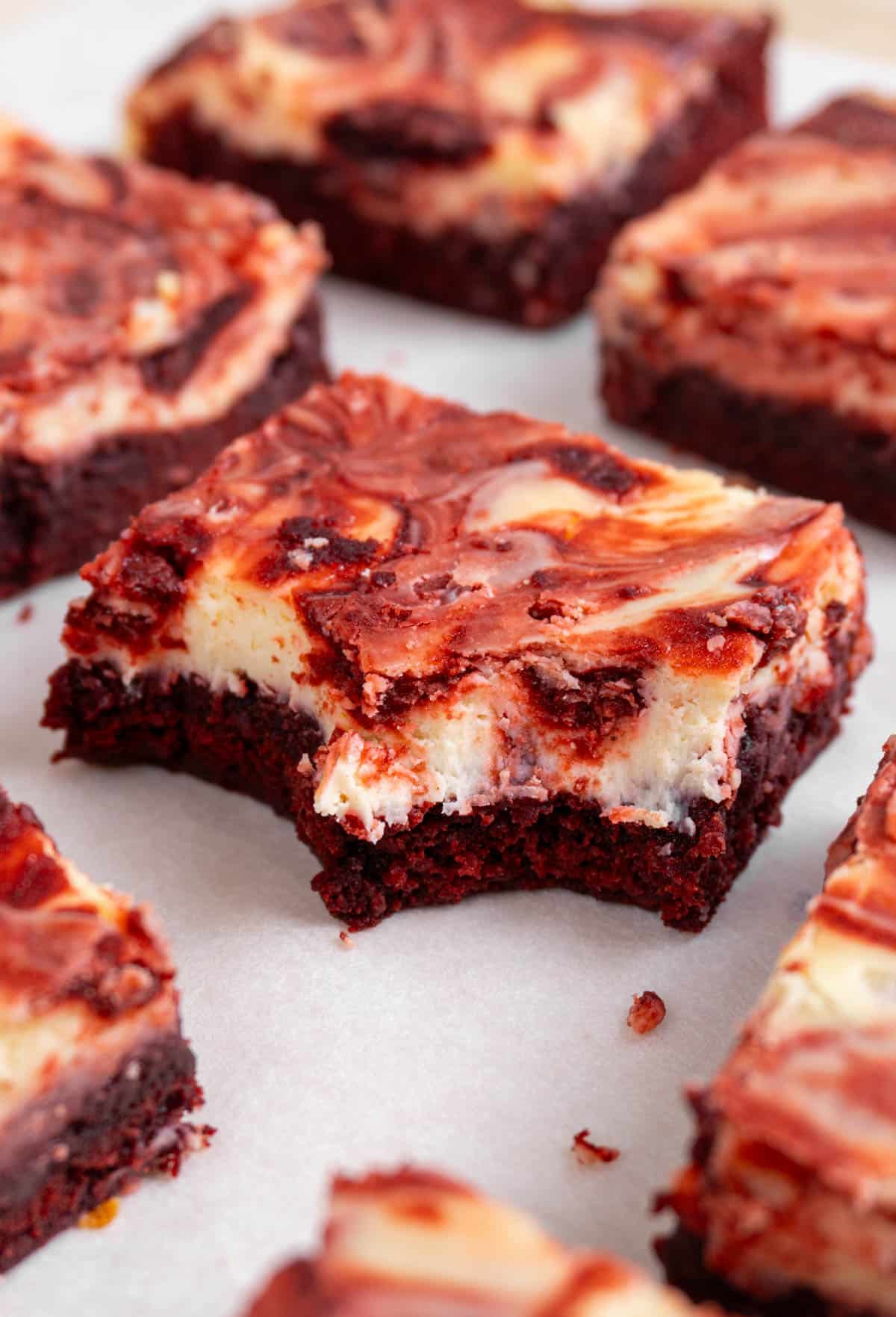 red velvet cheesecake brownies on a white surface. The middle one has 2 bites taken out of it