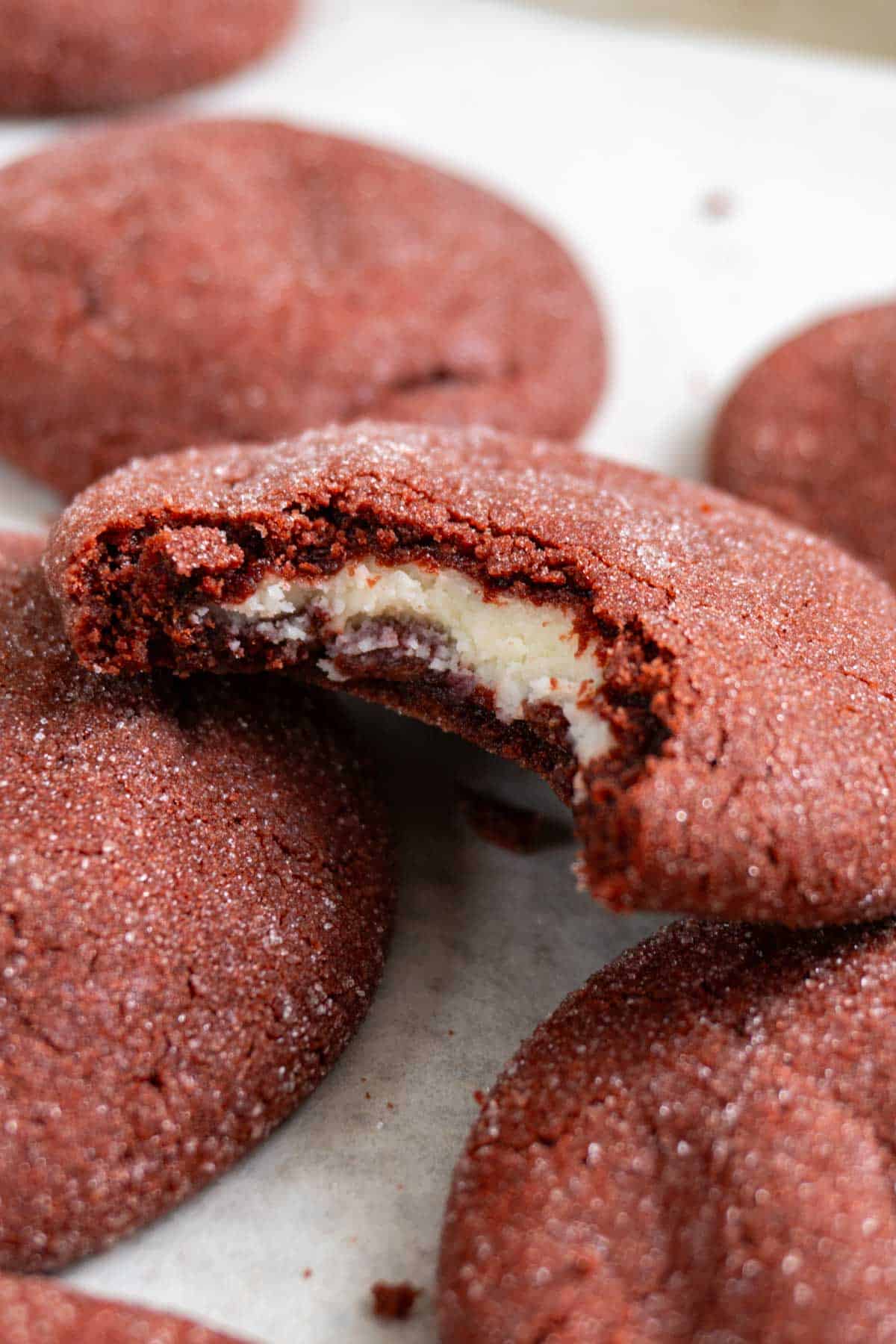 red velvet cookie that has a bite taken out of it, sitting on top of more cookies