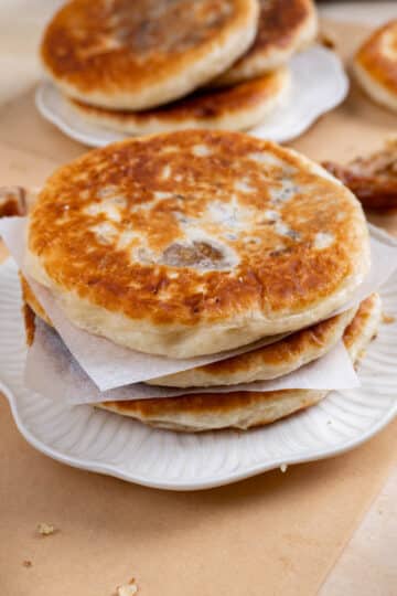 3 stacked hotteok on a white plate. Another plate with 3 more in the background