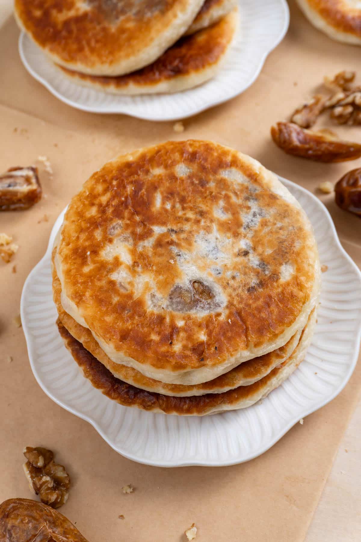 3 stacked hotteok on a white plate. Another plate with 3 more in the background