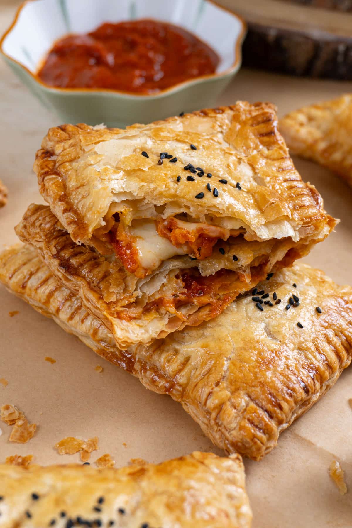 2 stacked pizza pockets on a brown parchment paper. A small  bowl with marinara sauce