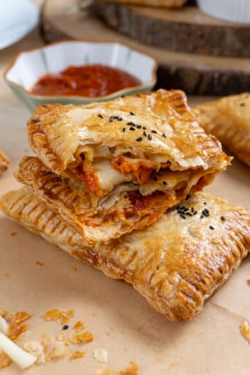 2 stacked pizza pockets on a brown parchment paper. A small bowl with marinara sauce