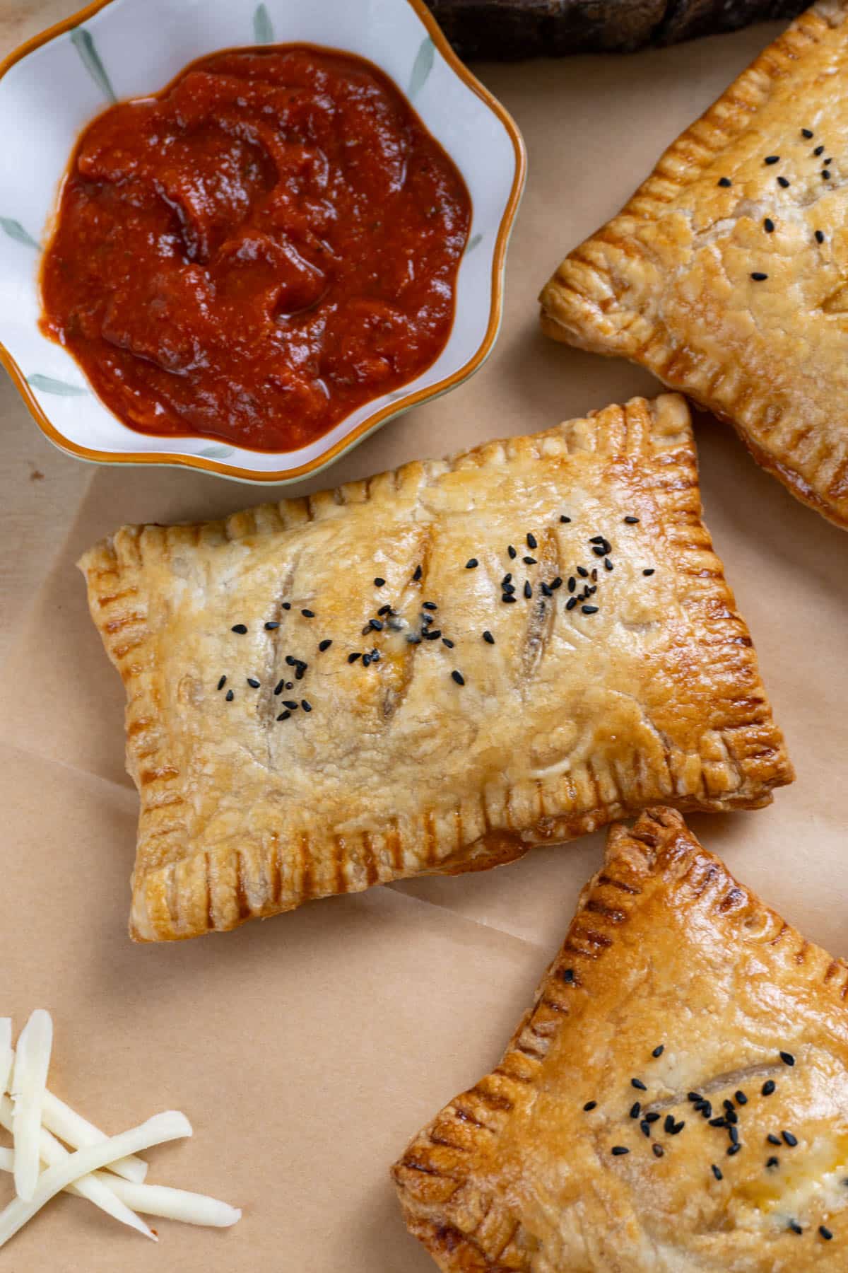 3 pizza pockets on a brown parchment paper. A small bowl with marinara sauce