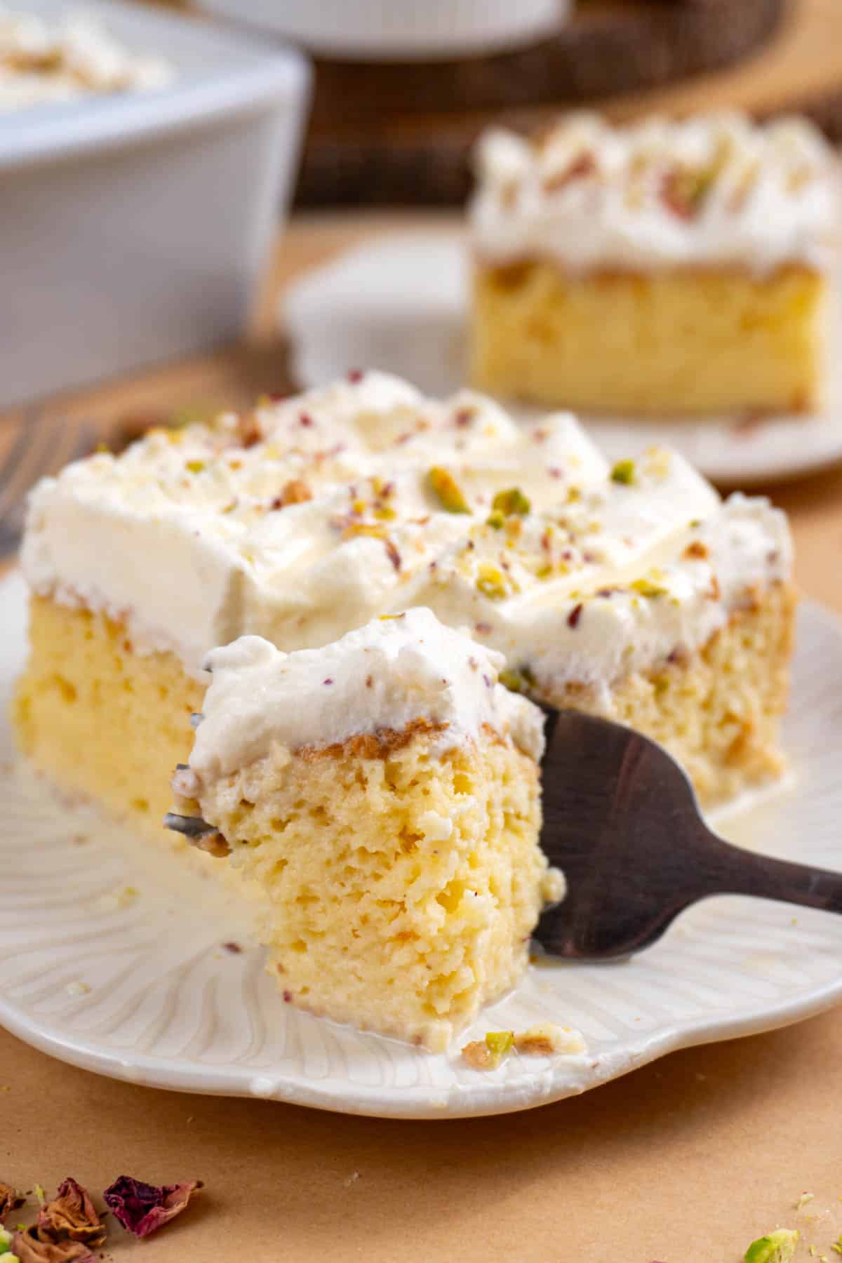 a slice of rasmalai tres leches on a white plate with a fork cutting into the cake