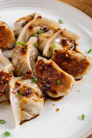 chicken potstickers on a white plate with chilli oil on top