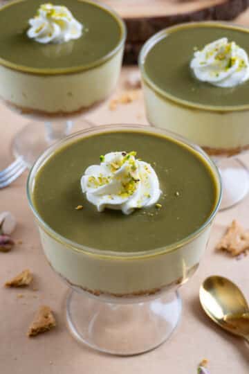 No bake pistachio cheesecake in a clear glass bowl. Two of them in the background