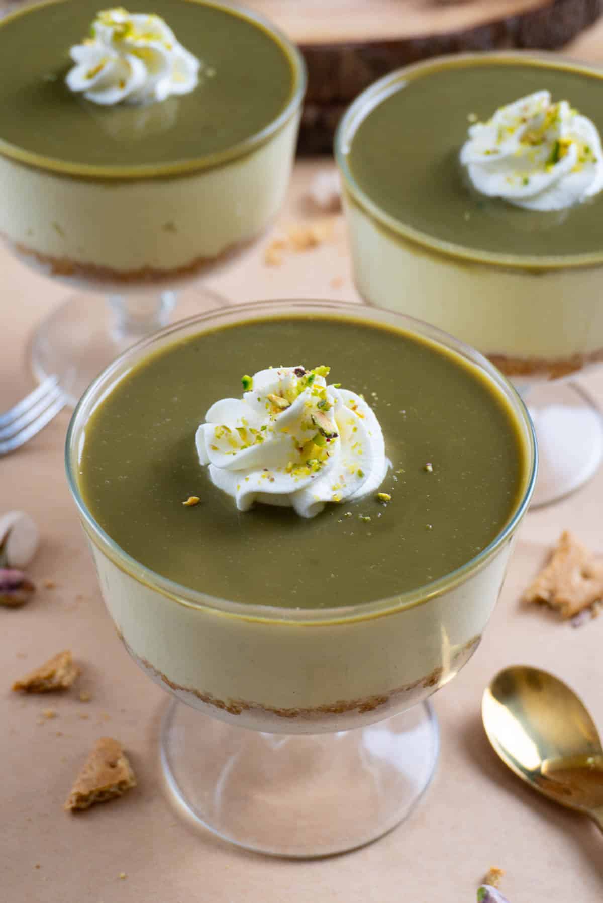 No bake pistachio cheesecake in a clear glass bowl. Two of them in the background
