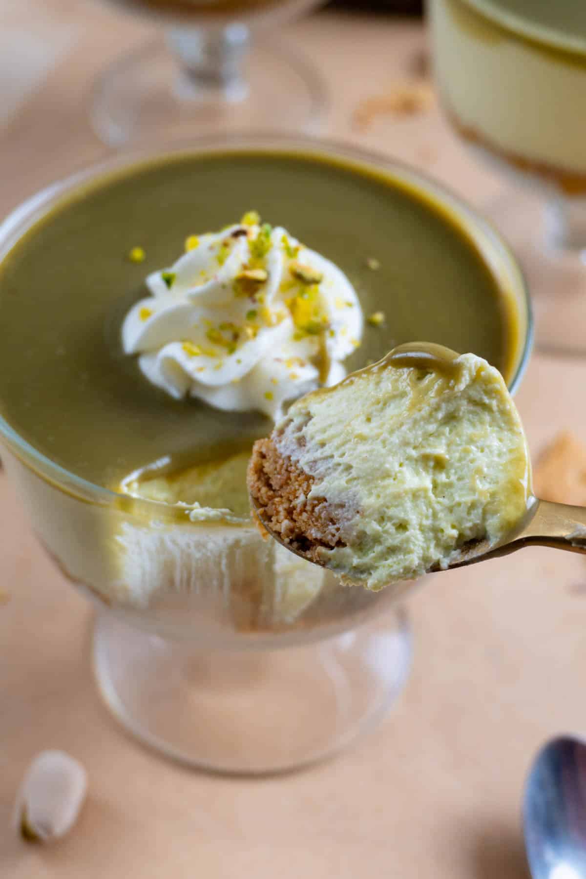 No bake pistachio cheesecake in a clear glass bowl with a spoon taking out a bite