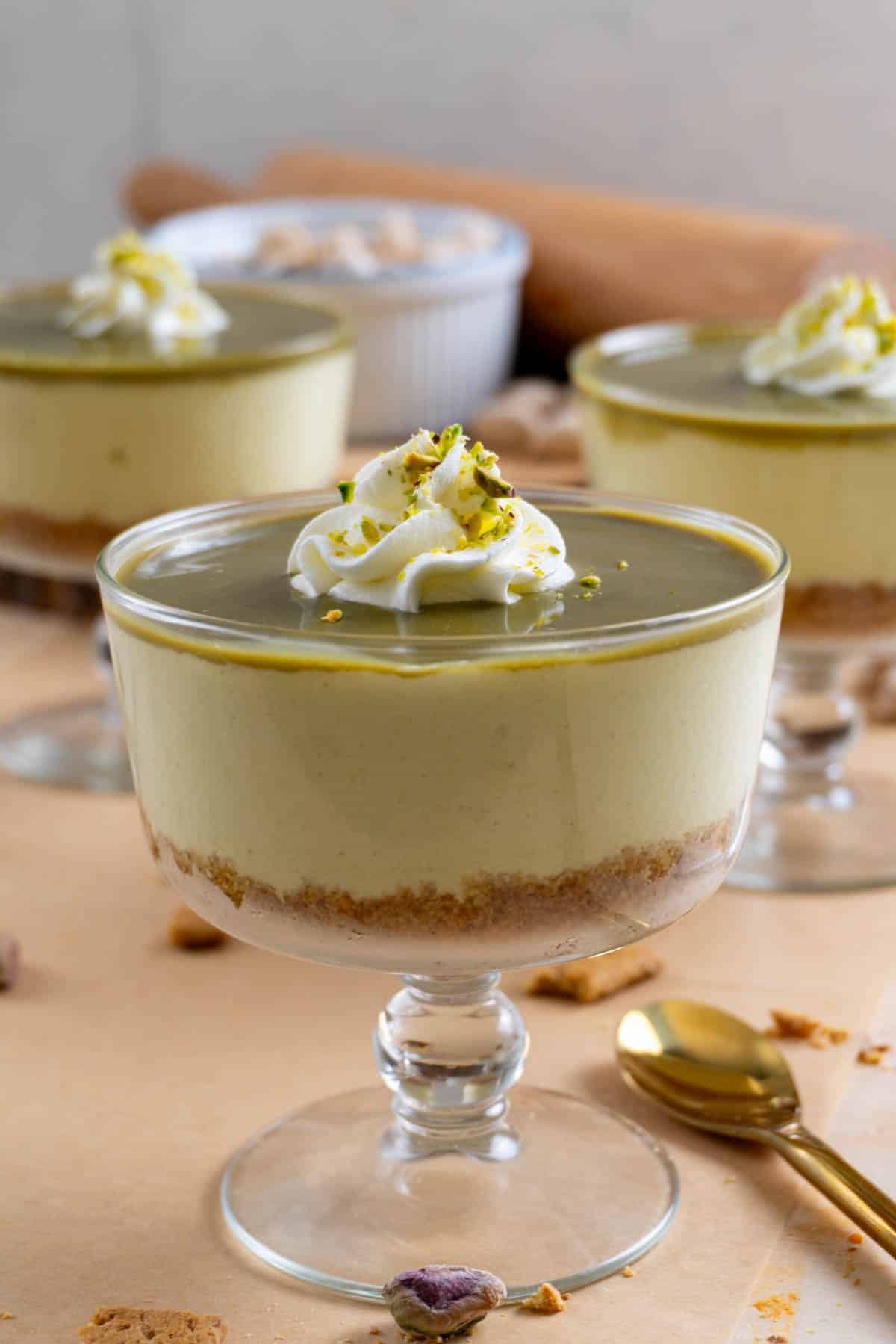 No bake pistachio cheesecake in a clear glass bowl. Two of them in the background