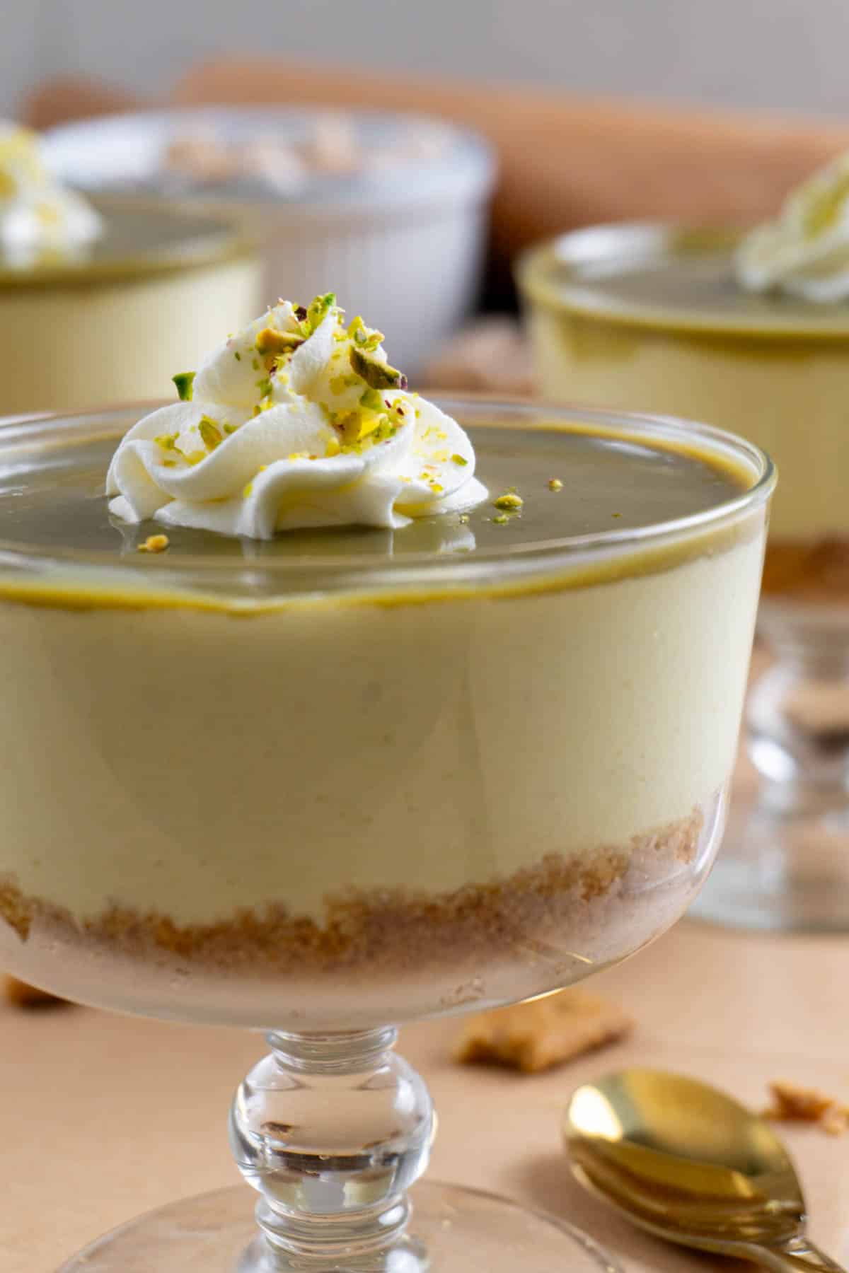 No bake pistachio cheesecake in a clear glass bowl. Two of them in the background