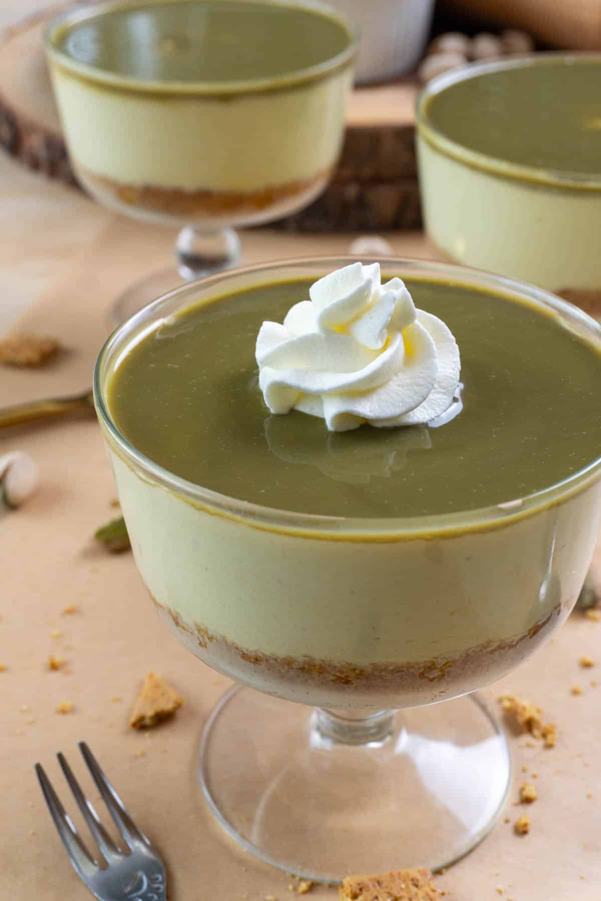 No bake pistachio cheesecake in a clear glass bowl. Two of them in the background