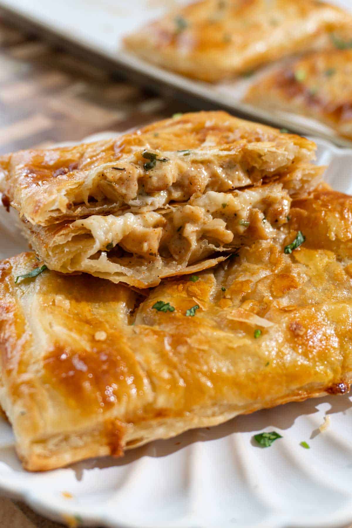 Chicken alfredo puff pastry on a white plate. One is cut in half and showing the cheesy chicken filling inside.
