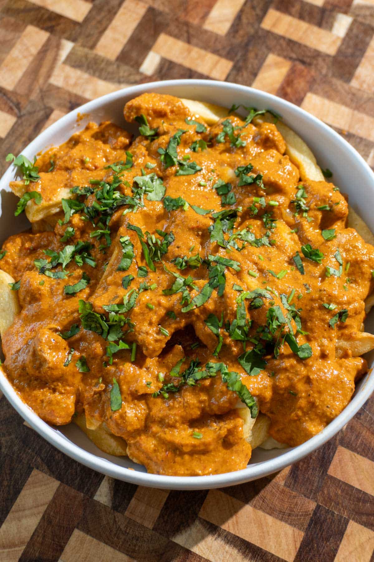 Butter chicken poutine in a dish set on a wooden cutting board