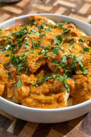 Butter chicken poutine in a dish set on a wooden cutting board