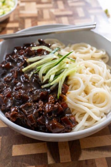 black bean noodles in a white dish, on a wooden cutting board