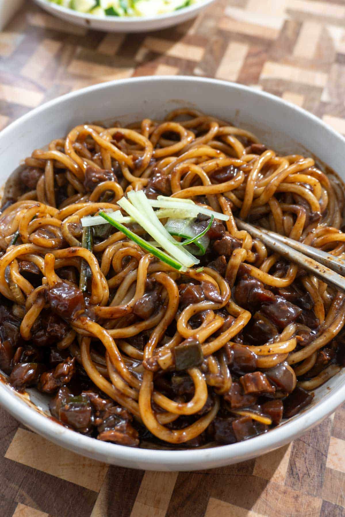 black bean noodles in a white dish, on a wooden cutting board